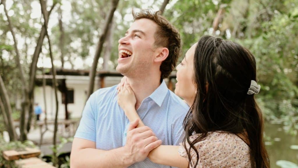 A man laughs loudly while a woman stands beside him with her hand on him.