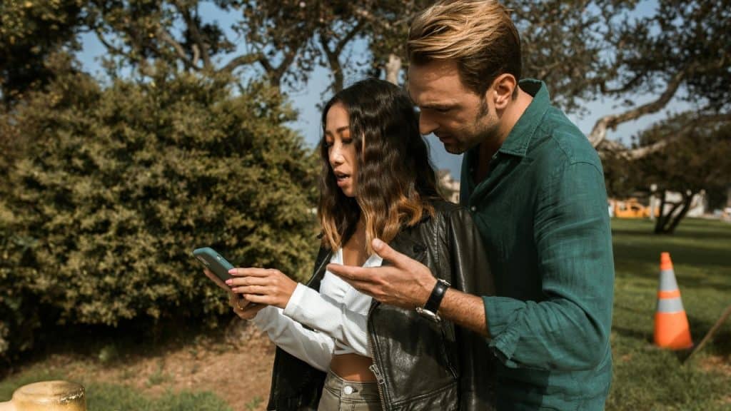 A man looks at a smartphone held by a woman in a black leather jacket.