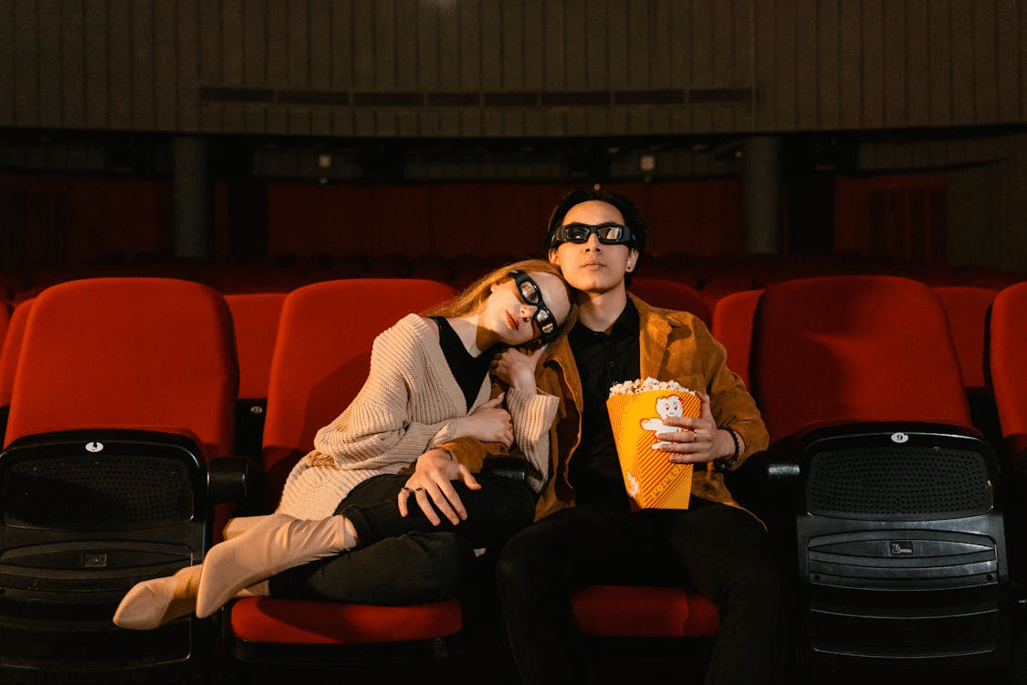 A Couple Sitting on Red Chairs with a Bucket of Popcorn