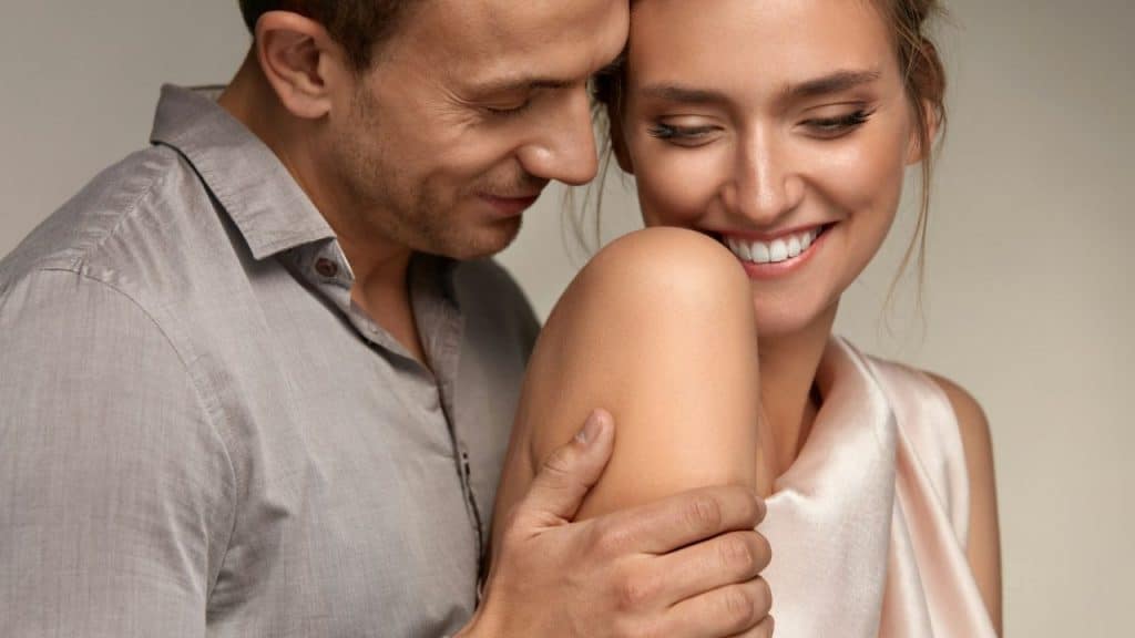 A man touching a woman's shoulder as they both look down and smile together.