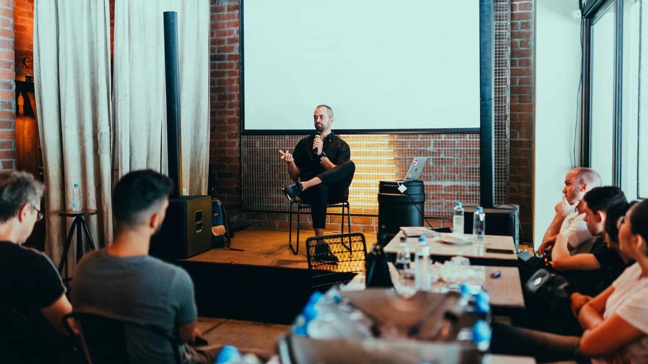 A man holding a mic speaking to a room full of people