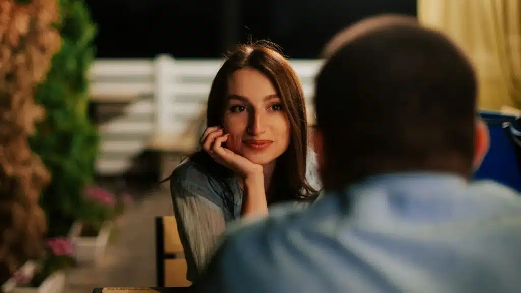 A woman rests her chin on her hand while looking at a man across a table.