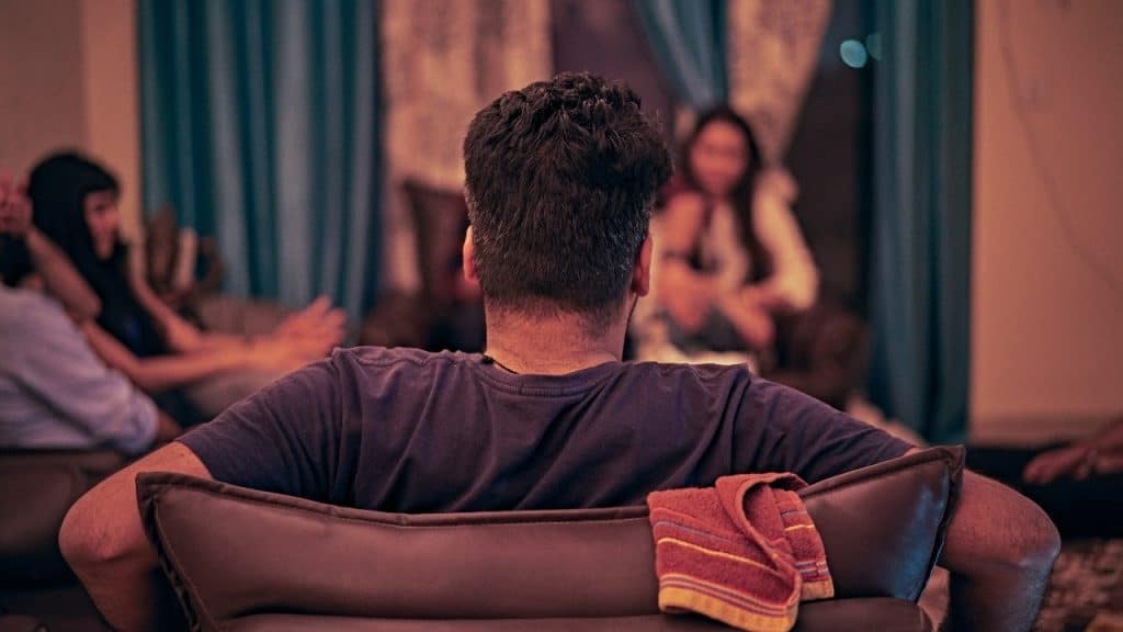 The back of a man's head as he sits on a chair looking toward other people.