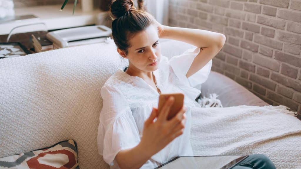 A woman sitting on a couch looking upset while checking her phone.