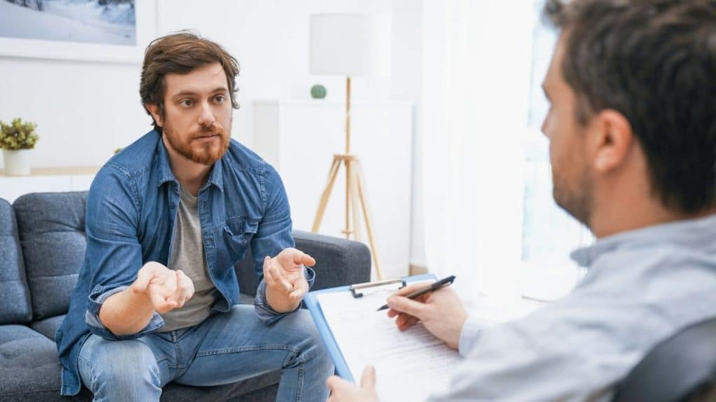 A man in a denim shirt talking to a person holding a clipboard and a pen.