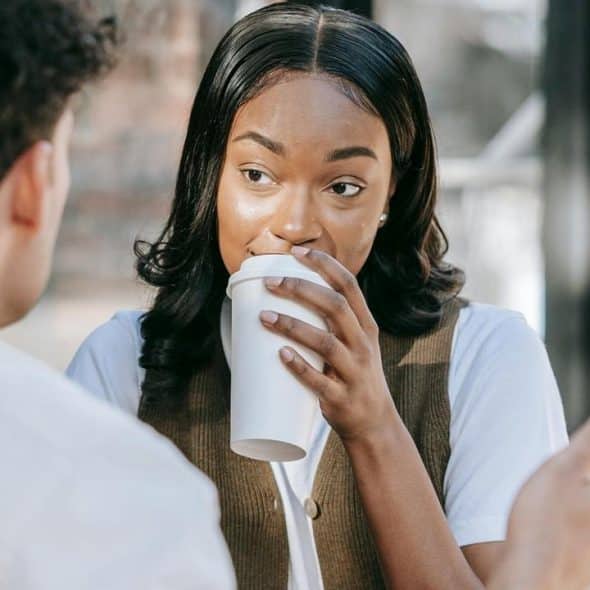 A woman is drinking coffee while talking to a man