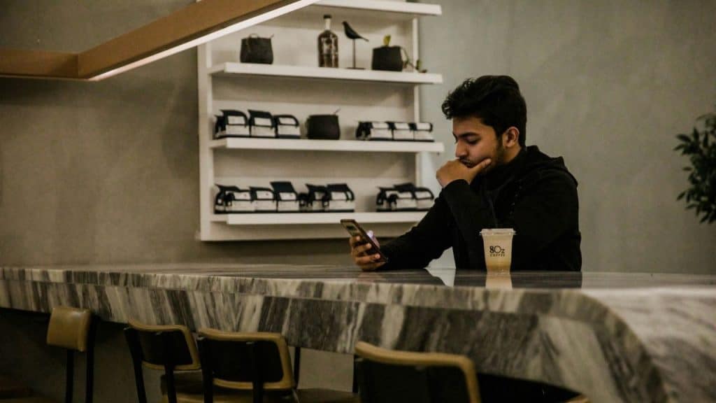 A man sitting at a marble counter looking at a smartphone next to a plastic cup.