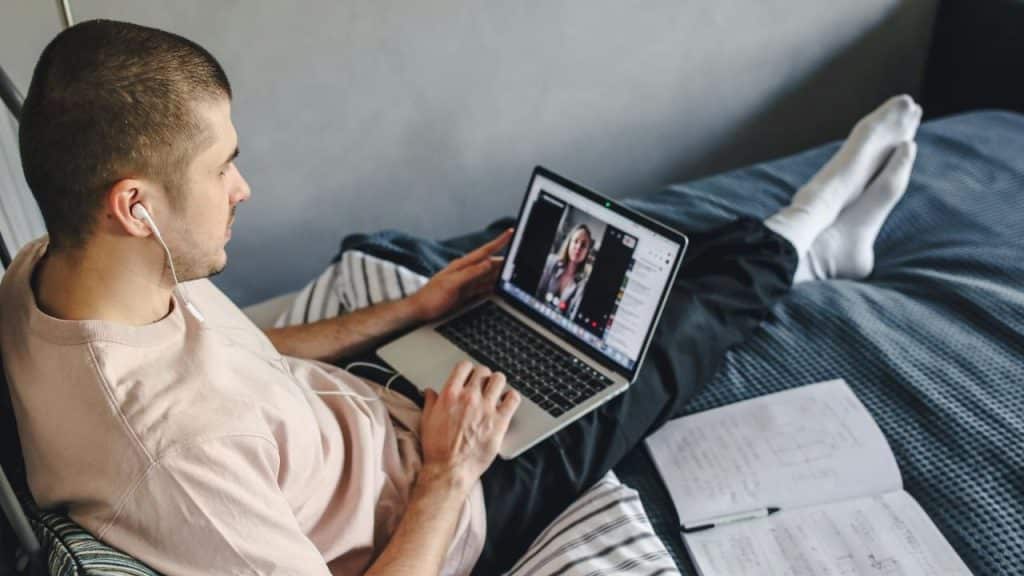 A man lying on a bed using a laptop for a video call with a woman.