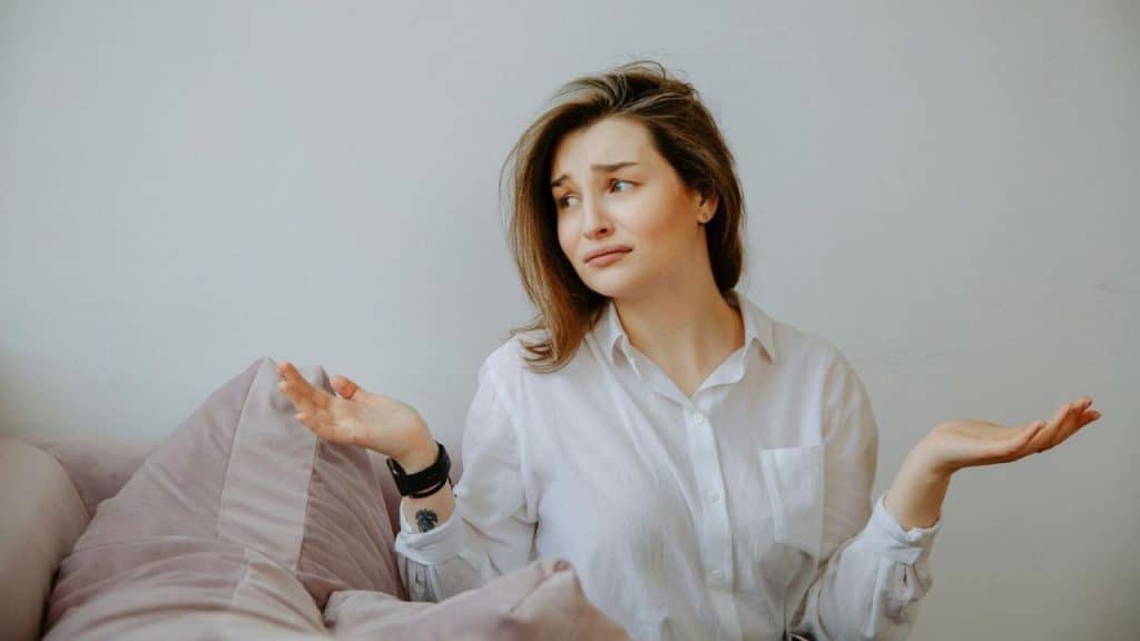 A woman in a white shirt sits on a couch with her palms facing upward.