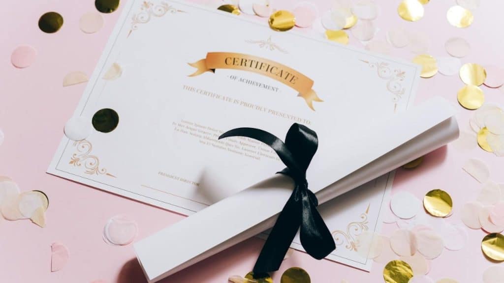 A formal certificate of achievement lies on a pink surface covered in gold confetti circles.