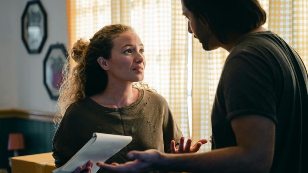 A woman holds a notebook and looks at a man who is gesturing with hands.