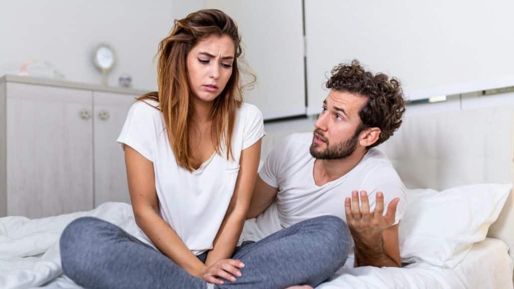 A woman looks down with a concerned expression while a man next to her gestures with one hand.