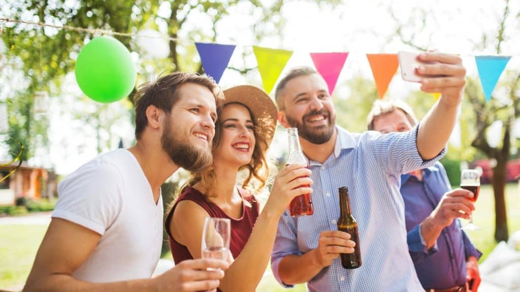A group of people smiling and holding drinks while taking a selfie at an outdoor party.