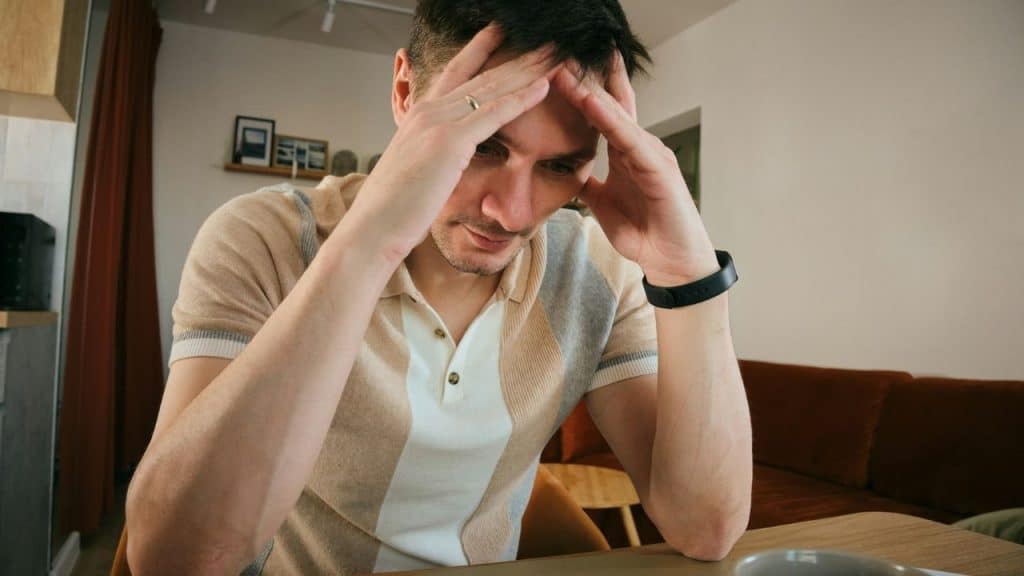 A man sits at a table with his head resting in his hands, looking down.