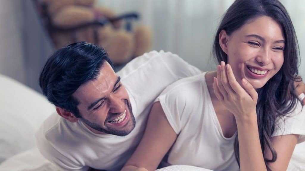 A man and woman are lying down and laughing together with their eyes closed.