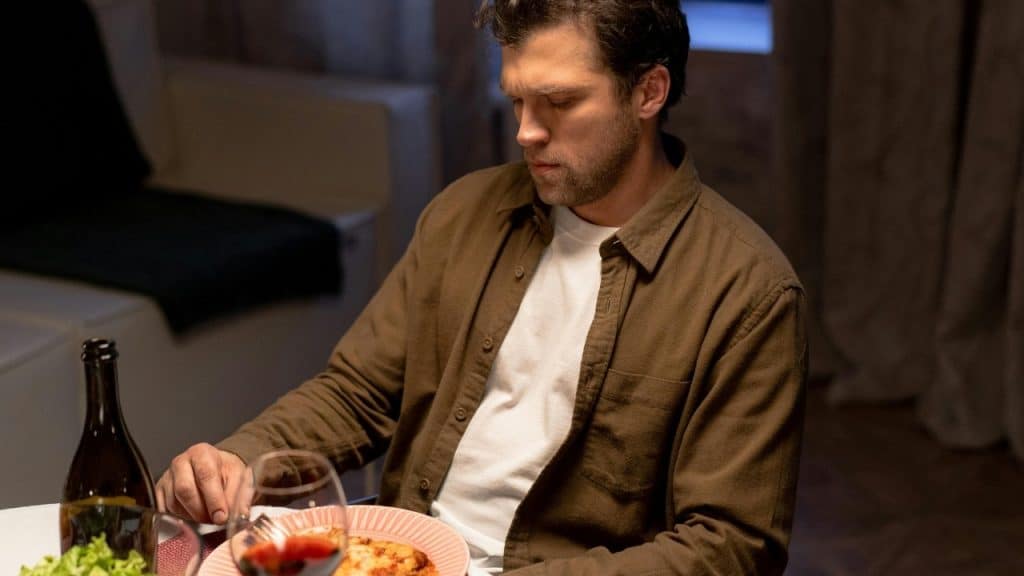 A man in a brown shirt sits at a dinner table with a plate of food.