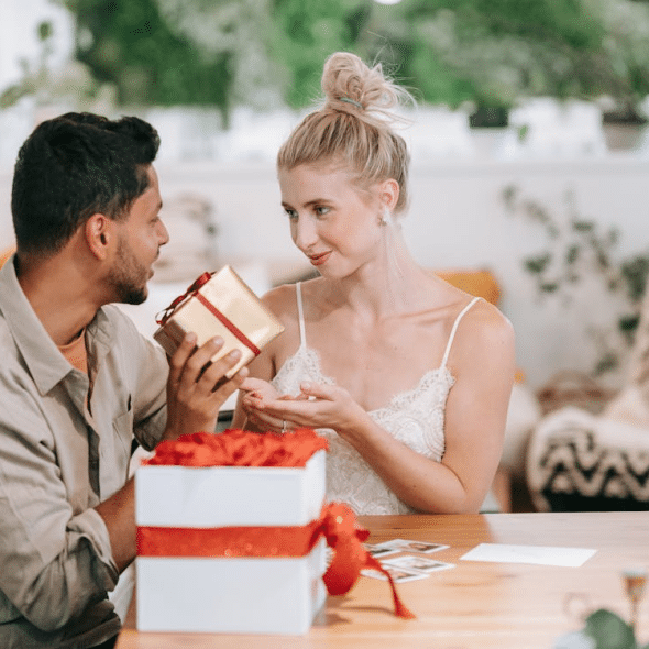 Man and Woman Sitting at Table and the man handing a gift to the woman.