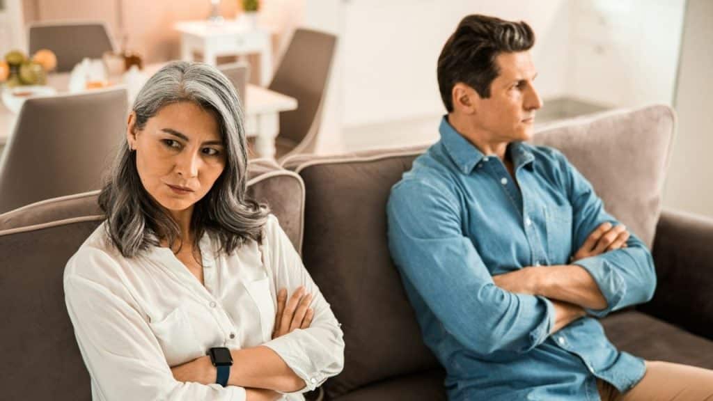 A woman and man sit on a couch with arms crossed, looking away from each other.