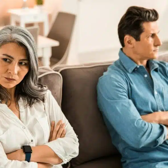 A woman and man sit on a couch with arms crossed, looking away from each other.