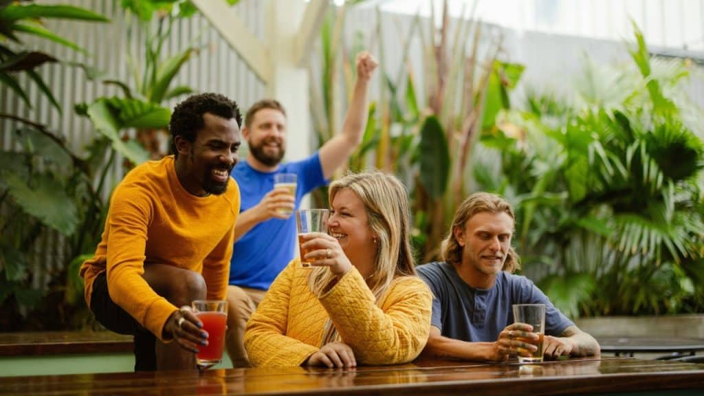 Four people sit at an outdoor wooden table, smiling and holding glasses of beer.