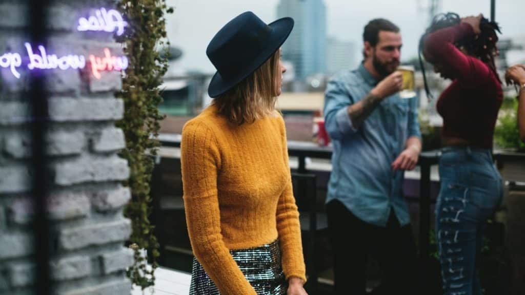 A woman in a hat looks away from a man drinking a beer at a party.
