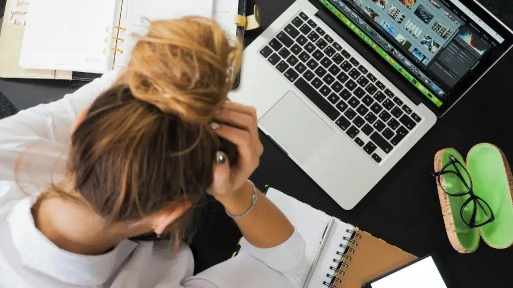 Overhead view of a woman with her head in her hands at a desk with a laptop.