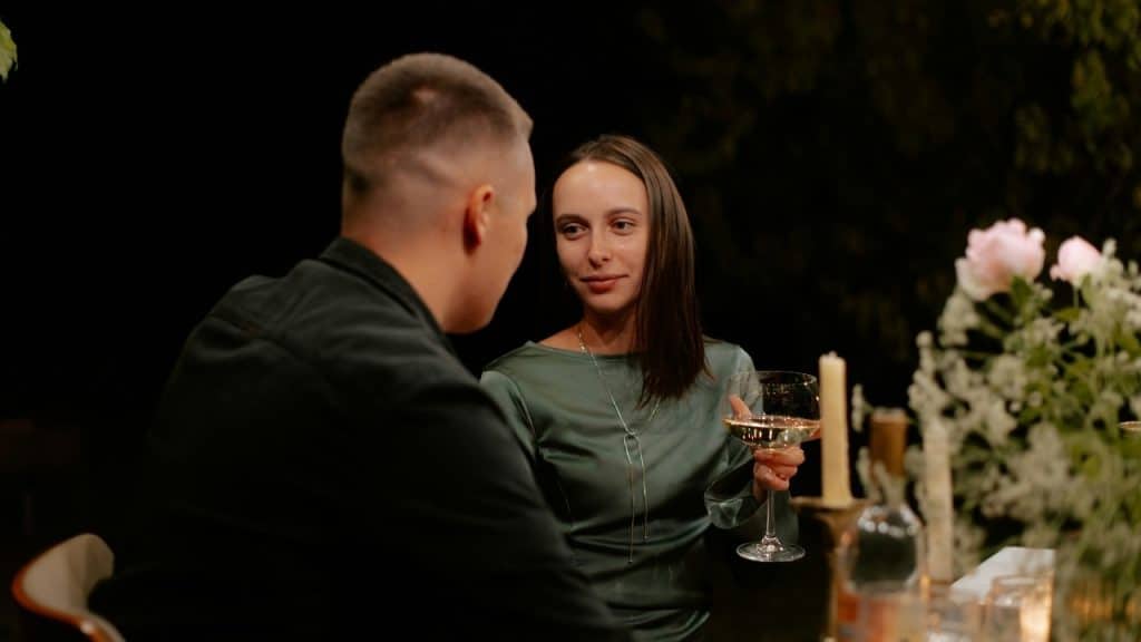 A woman in a green dress holds a wine glass while looking at a man.