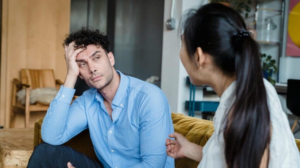 A man with curly hair leans his head on his hand while looking at someone.