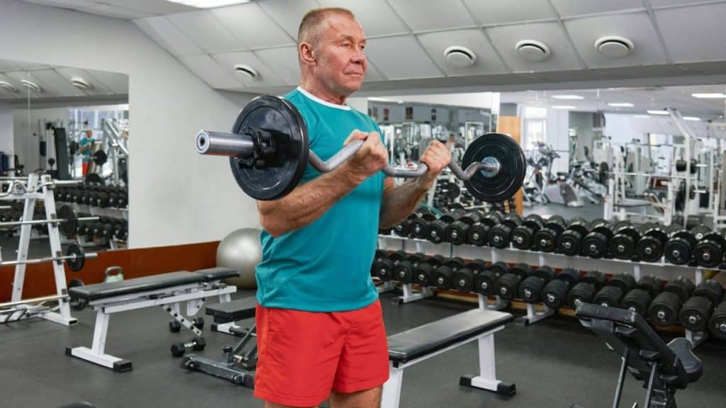A man in a teal shirt and red shorts lifts a barbell in a gym setting.