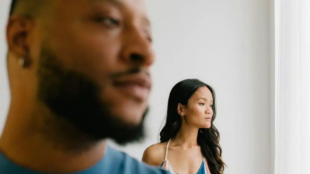 A couple standing seprately are looking at one side of the room.
