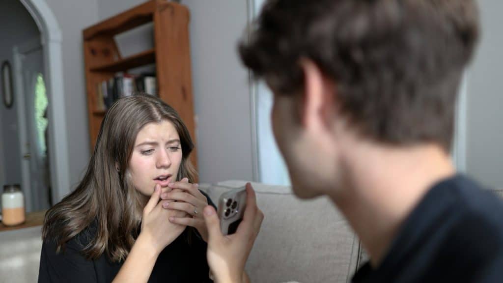 A man showing something to his wife on phone and woman is covering her face with her hands.