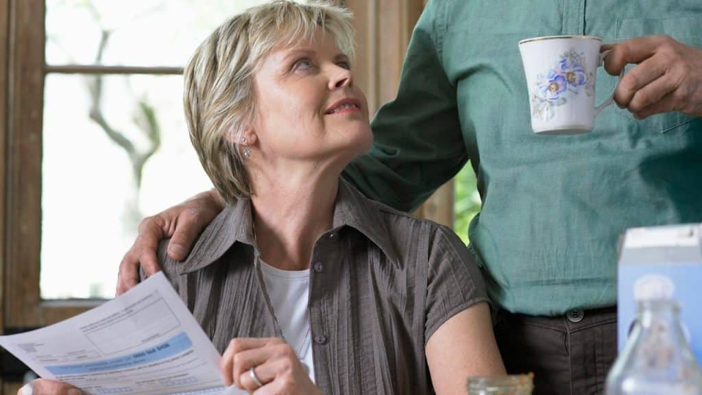 A woman holding a financial paper looking at his husband, who is standing behind him.
