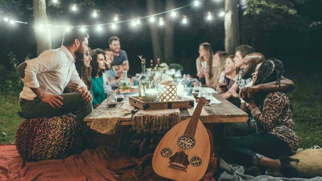 A diverse group of friends sitting at a dinner table with a musical instrument lying alongside it.