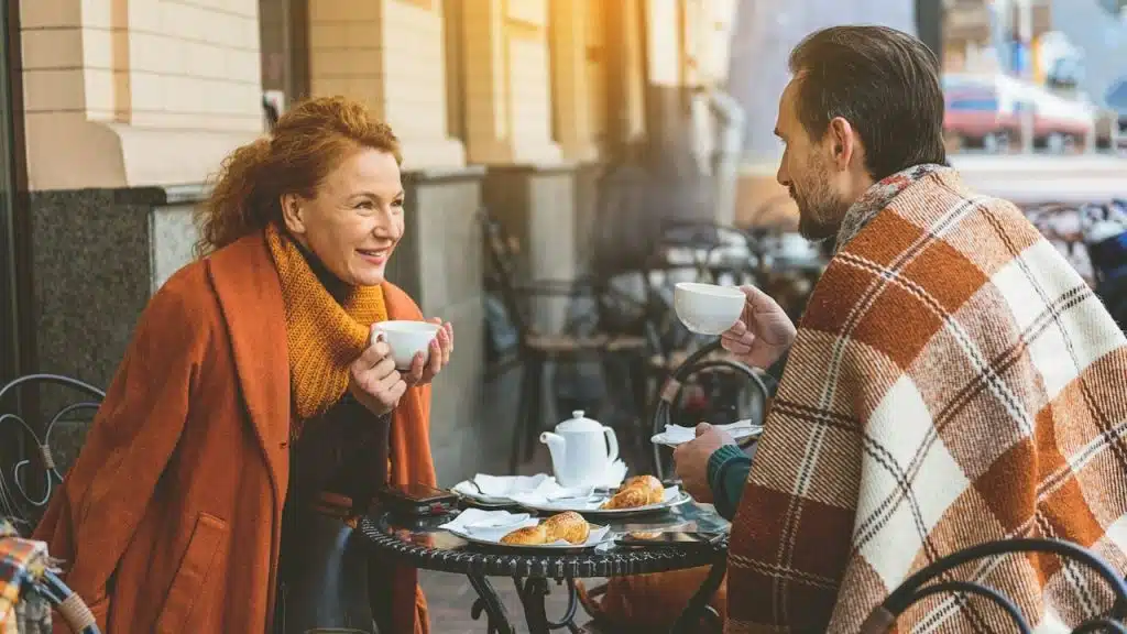 Couple is drinking tea and talking in cafe outdoors they are looking at each other with love and smiling.