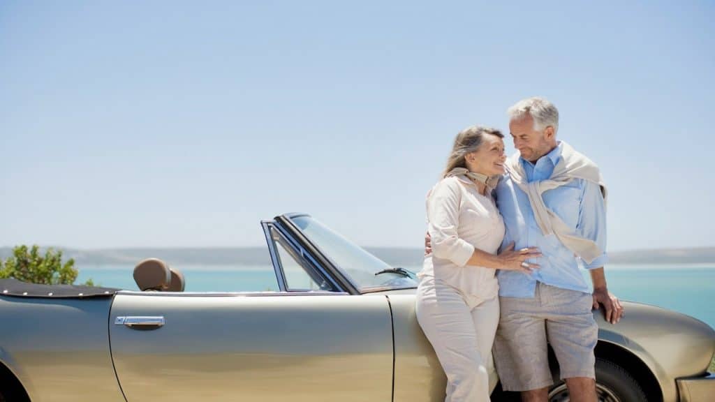A senior couple standing next to their luxary car near a body of water.