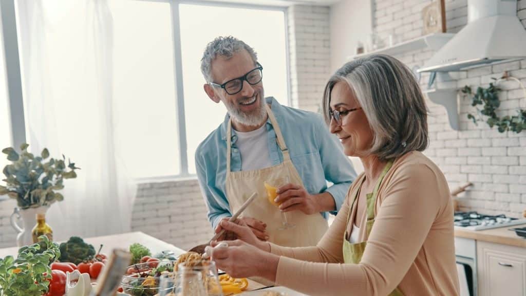 A senior couple in aprons preparing  healthy dinner and smiling while spending time at home.