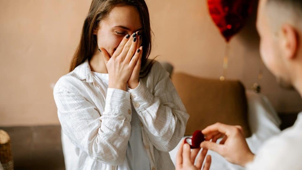 A man giving a wedding to a woman, woman covering her face with her hands out of joy.