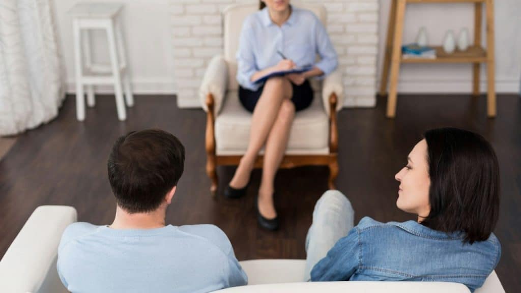 A depressed unhappy young couple sitting opposite to a psychologist and describing their problems while having an appointment.