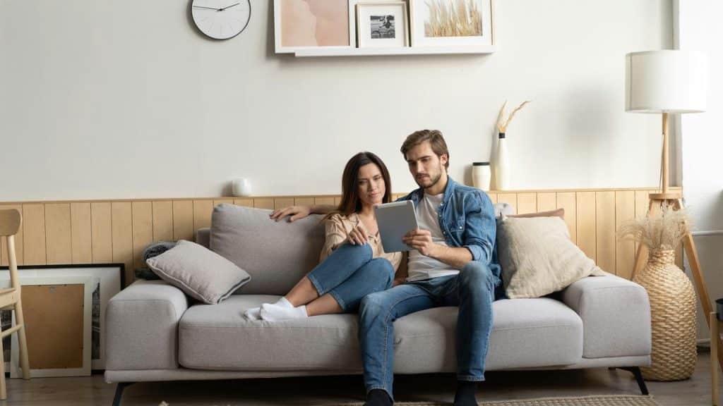 A couple sitting together on a couch while looking at a tablet.