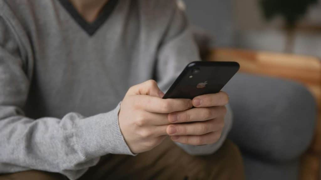 A person's hands are shown in a close-up holding and using a black smartphone indoors.