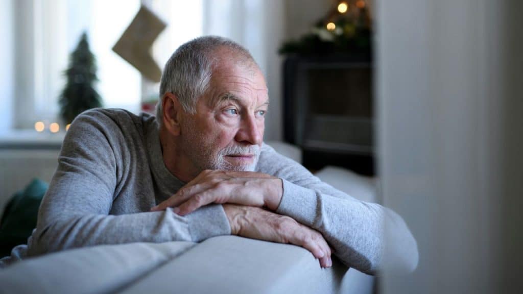 A man leaning his chin on his crossed arms while looking out of a window.