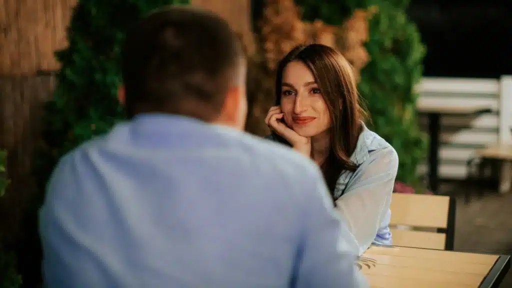 A woman rests her chin on her hand while looking at a man's back.