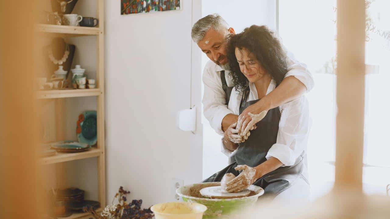 A couple happily working together on pottery at a pottery wheel.