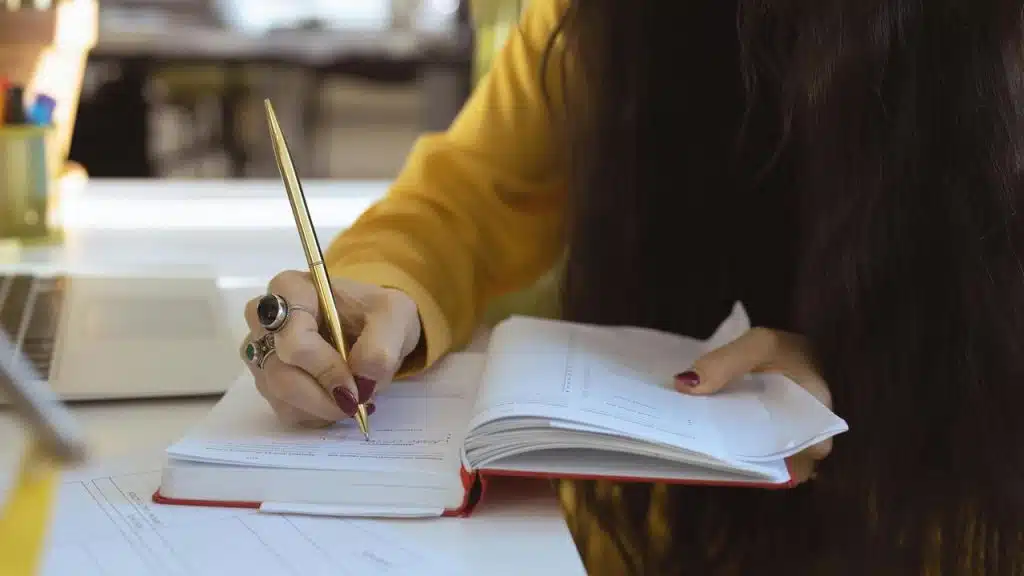 A person writing in a notebook at a desk.