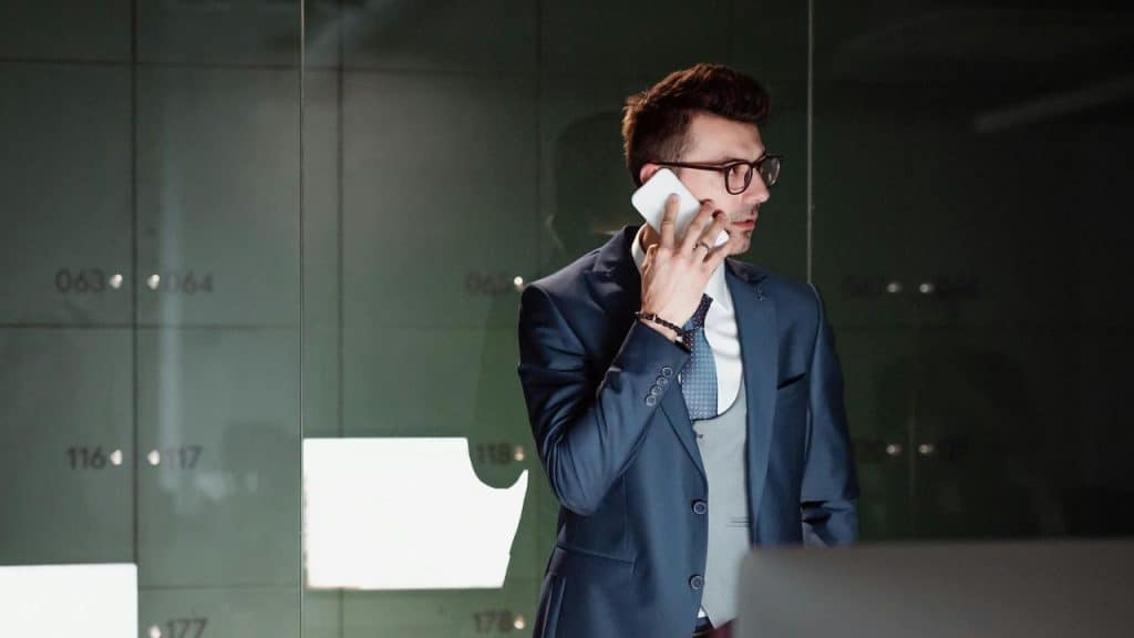 A man in a suit talking on a smartphone in a modern office setting.