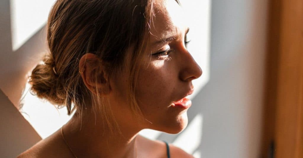 A woman in side profile lit by warm sunlight indoors.