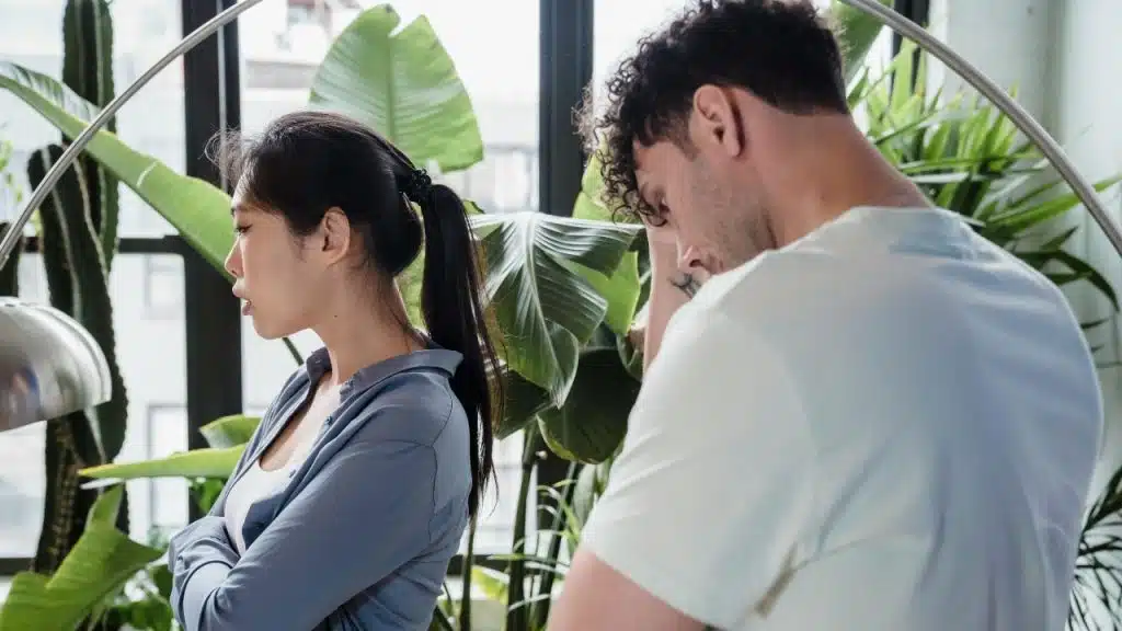 A woman stands with crossed arms looking away from a man who is looking down.