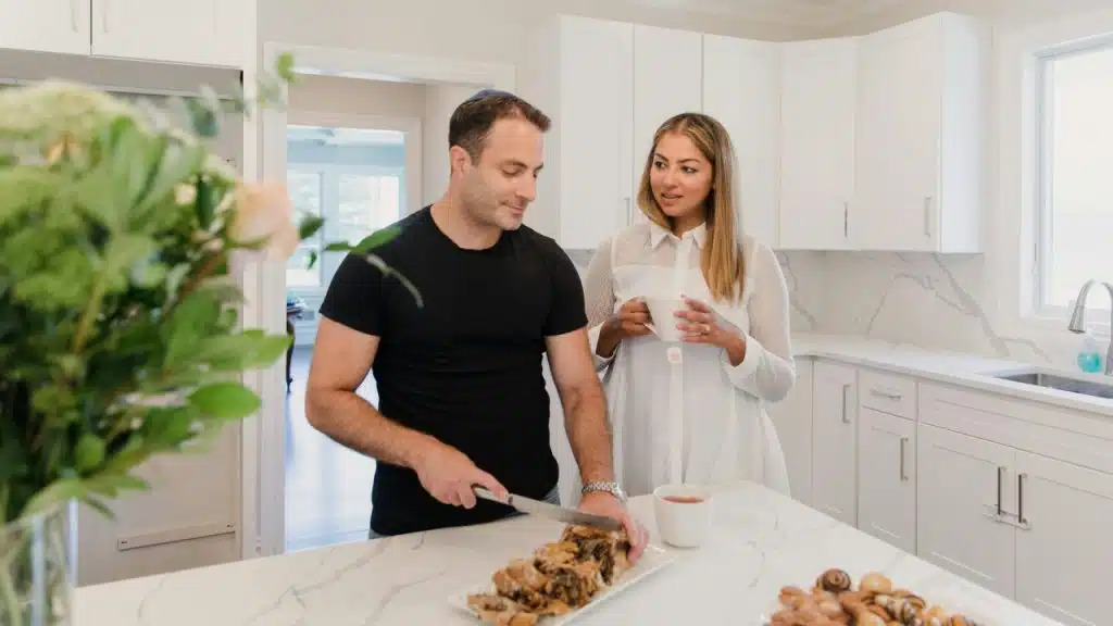 Man cutting a loaf of bread on a counter while a woman watches holding a mug.