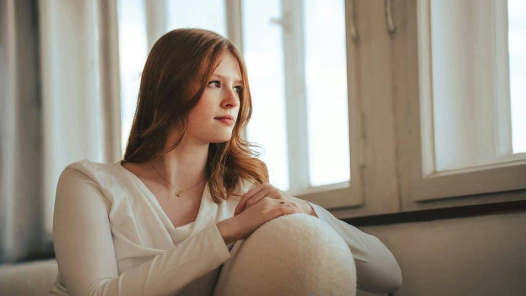 A person sitting by a window, looking outside thoughtfully.