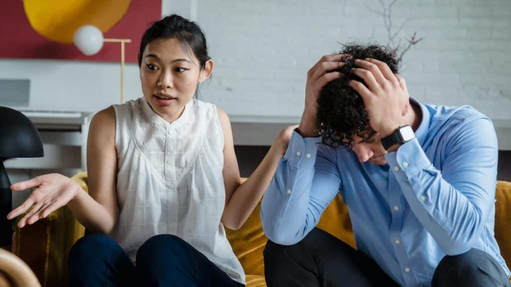 A woman with her hand out talks to a man who is holding his head.